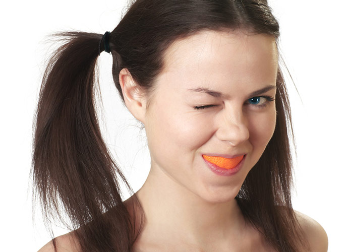 Young woman with an orange peel in her mouth