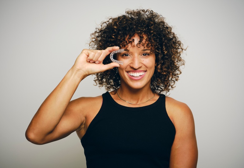 : A smiling woman holding an Invisalign clear aligner, promoting orthodontic treatment in Homewood, IL